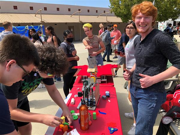 Student with red hair smiling as students try to solve a puzzle